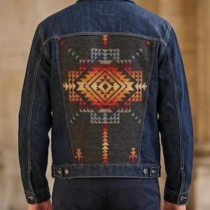 May include: A dark wash denim jacket with a decorative patterned back panel. The panel features a geometric design in shades of orange, red, and blue on a gray background. The jacket has button closures and pockets.