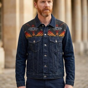 May include: A dark blue denim jacket with a patterned yoke featuring orange, red, and gray geometric designs. The jacket has silver buttons and two chest pockets. The model is wearing dark blue pants.