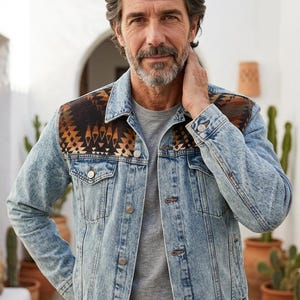 May include: A light blue acid-wash denim jacket featuring a dark brown and black geometric patterned fabric panel across the shoulders and chest, a classic collar, metal button closures, and two chest pockets with buttoned flaps.