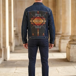 May include: Dark wash denim jacket with a colorful geometric design on the back. The design features shades of red, orange, yellow, and blue. The jacket has a classic collar, button closures, and pockets.