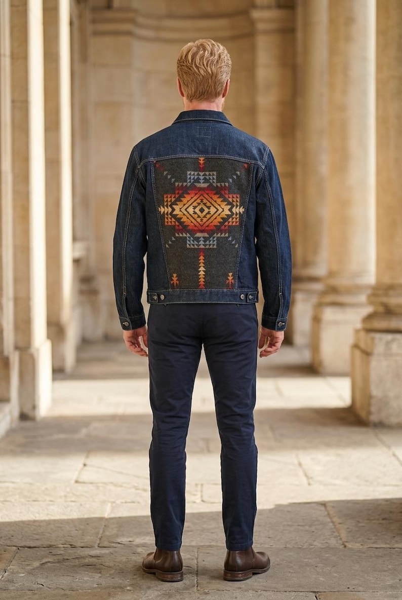 May include: Dark wash denim jacket with a colorful geometric design on the back. The design features shades of red, orange, yellow, and blue. The jacket has a classic collar, button closures, and pockets.
