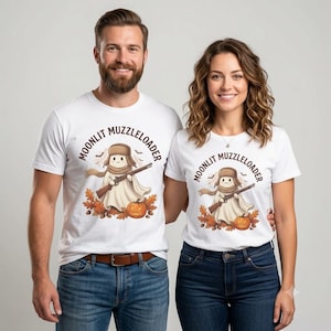 May include: A white t-shirt featuring a graphic of a ghost wearing a brown trapper hat and scarf, holding a muzzleloader rifle. The design includes autumn leaves, a jack-o'-lantern, and bats, with the text MOONLIT MUZZLELOADER arched above.