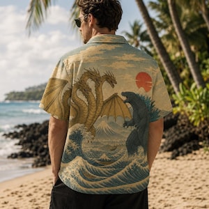 Puede incluir: Una camisa de manga corta con botones frontales sobre un fondo beige, con un estampado gráfico de un dragón de tres cabezas y un monstruo grande frente a frente sobre olas del mar, una montaña y un sol de color rojo.