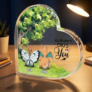 May include: A heart-shaped acrylic block featuring a butterfly and a dragon-like creature, with the names "ROSA" and "JOHN" below. The block has a tree and grass design, with the text "I'LL ALWAYS CHU'S You".