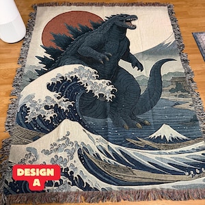 Può includere: Una coperta tessuta con un design di Godzilla con un motivo a onde giapponesi, un sole rosso e una montagna. La coperta ha un bordo con frange e il testo "DESIGN A" in un riquadro rosso.