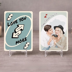 Puede incluir: Dos tarjetas personalizadas de San Valentín sobre soportes transparentes. Una tarjeta dice "Love You More" con los nombres "Anthony" y "Anna". La otra muestra una pareja con tazas de café y el texto "Happy Valentine Day 2026".