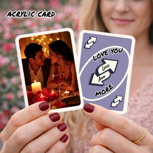 Puede incluir: Se muestran dos tarjetas acrílicas, una con una escena de cena romántica con una pareja, velas y rosas. La otra tarjeta tiene un fondo morado con las palabras "LOVE YOU MORE" y flechas. El texto "ACRYLIC CARD" está en la parte superior.