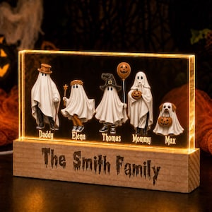 May include: A rectangular acrylic light display featuring five ghost figures and a dog ghost, each labeled with names: Daddy, Elena, Thomas, Mommy, and Max. The base is wood with the text The Smith Family engraved on the front. The display glows orange.