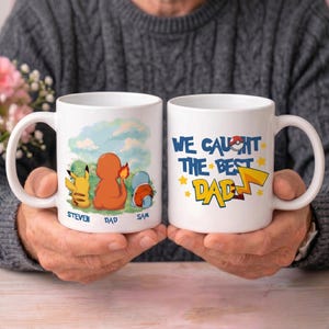 May include: Two white ceramic mugs featuring colorful illustrations. One mug shows Pikachu, Charmander, and Squirtle with the names Steven, Dad, and Sam. The other mug displays the text WE CAUGHT THE BEST DAD with yellow stars and a lightning bolt.