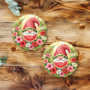 May include: Two circular car coasters featuring a gnome illustration. The gnome wears a watermelon-patterned hat and holds a slice of watermelon. The design is surrounded by a colorful wreath of red poppies, pink hibiscus, and white daisies.