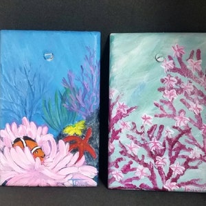 May include: Two small paintings on canvas depicting underwater scenes. The left painting shows a clownfish in a pink anemone with coral and a starfish. The right painting shows a pink coral reef with white flowers.