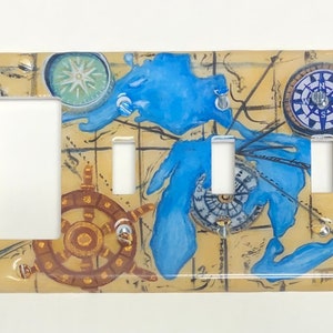 May include: A light switch cover with a nautical map design. The cover features a compass, a ship's wheel, and a blue lake. The compass points north, south, east, and west. The switch cover is labeled with the directions NW, NE, SW, and SE.
