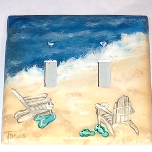 May include: A hand-painted light switch cover with a beach scene. The cover features two beach chairs, flip flops, and a blue ocean with white waves. The words "TDavis" are signed in the bottom left corner.