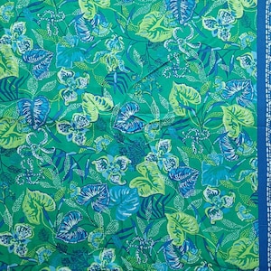 May include: Green fabric with a vibrant floral and leaf pattern in shades of blue and green. The design includes stylized flowers and large leaves, with a blue border on the right side. The fabric is suitable for various sewing projects.
