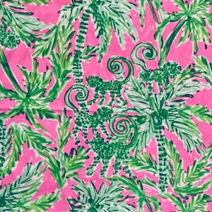 May include: A vibrant pink fabric featuring a repeating pattern of green palm trees and stylized monkeys. The design includes swirling accents and varying shades of green, creating a tropical theme.