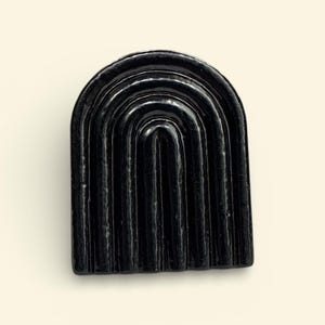 May include: A shiny black cabinet knob with an arched rainbow design. The knob features vertical lines and a curved top. This modern hardware is suitable for drawers or cabinets.