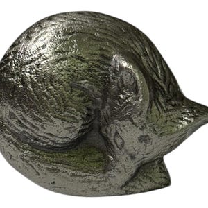 Pode incluir: Estatueta decorativa de gato prateado em posição de dormir enroscado. O pelo do gato tem uma aparência texturizada, e a estatueta está sobre um fundo branco. Adequado para decoração de casa.