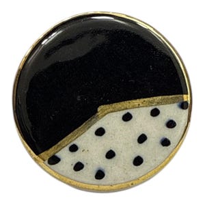 Könnte beinhalten: Runder, dekorativer Ansteck-Pin mit goldfarbenem Rand. Die Oberfläche des Pins ist diagonal geteilt, mit einer schwarzen oberen Hälfte und einer unteren Hälfte in Weiß mit schwarzen Tupfen. Das Design ist schlicht und modern.