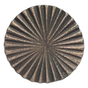 May include: A circular, bronze-toned decorative item with a textured, ridged surface. The ridges extend from the centre, forming a sunburst design. The object has a slightly irregular, organic edge, and is set against a white background.