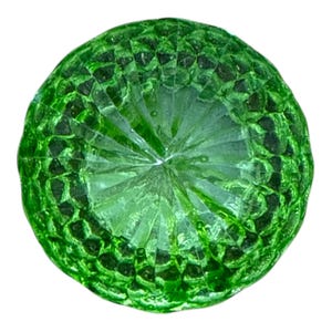 May include: A round, faceted, emerald-green glass object. The object has a textured surface with a pattern of small, raised geometric shapes around the edge. The center has a starburst design.