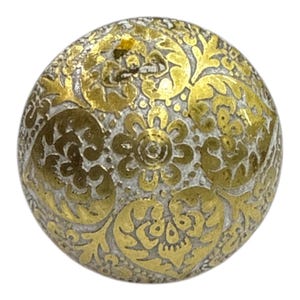 May include: A round button with a silver base and gold floral filigree design. The button features intricate patterns of stylized flowers and leaves, creating a vintage aesthetic. This decorative button is ideal for clothing or craft projects, adding a touch of elegance.