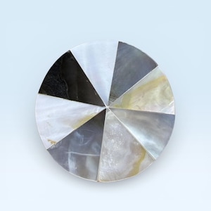 Puede incluir: Un objeto decorativo redondo con un diseño segmentado. Los segmentos son triangulares y están dispuestos en un patrón circular. Los colores incluyen blanco, negro, gris y un toque de dorado. El objeto parece estar hecho de un material reflectante.