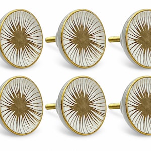 May include: A set of six round cabinet knobs featuring a white surface with a gold sunburst pattern radiating from the center. Each knob has a gold-toned metal rim and a matching gold-toned threaded bolt extending from the back for installation.