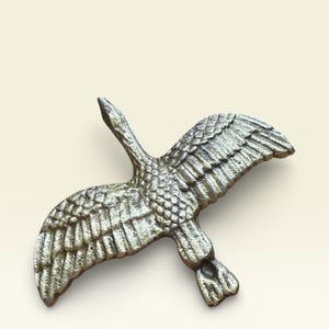May include: A detailed, metallic sculpture of a goose in flight. The wings are outstretched, showcasing intricate feather detailing. The sculpture has a silver finish and is set against a neutral background.