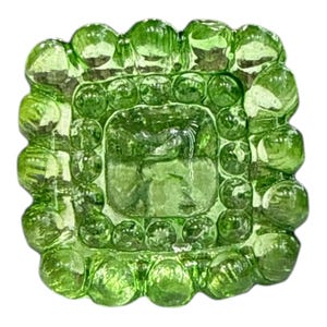 Puede incluir: Un objeto cuadrado de vidrio verde claro con una superficie texturizada. El centro tiene forma cuadrada, rodeado de pequeñas burbujas de vidrio redondas. Los bordes están revestidos con piezas de vidrio más grandes en forma de burbuja.