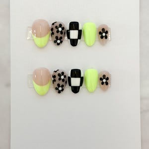 May include: A set of press-on nails with a variety of designs. The nails feature a combination of colors, including neon yellow, black, and nude. Some nails have a black and white checkerboard pattern, while others have black flower designs.