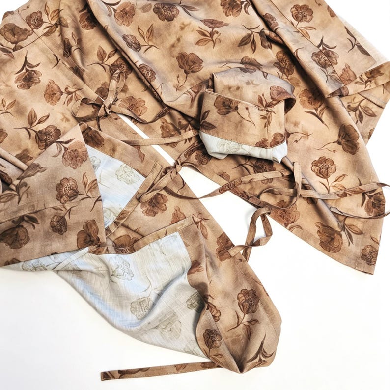 K&ouml;nnte beinhalten: Ein beigefarbener Wickelstoff mit dunkelbraunem Blumenmuster, das St&auml;ngel und Bl&auml;tter zeigt. Das Kleidungsst&uuml;ck verf&uuml;gt &uuml;ber d&uuml;nne Stoffb&auml;nder zum Binden und eine hellere, cremewei&szlig;e Innenseite mit einem dezenten, blassen Blumenmuster.