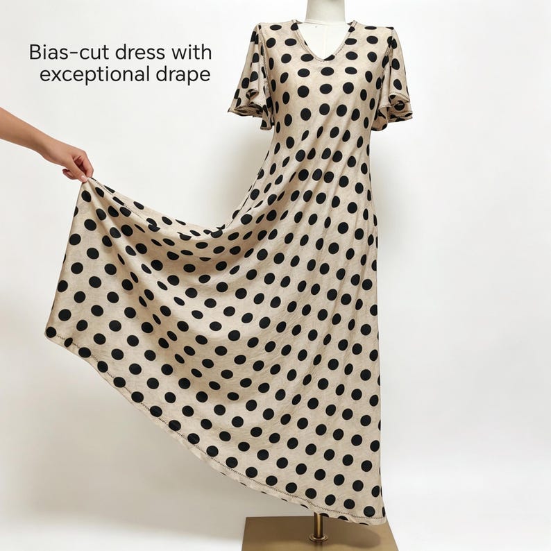 May include: A beige bias-cut dress featuring a black polka dot pattern, short flutter sleeves, and a V-neckline. The text Bias-cut dress with exceptional drape is printed on the upper left side of the image, describing the garment's silhouette.
