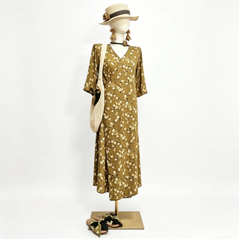 May include: A mannequin displays a floral print dress, straw hat, earrings, and a woven tote bag. The olive green dress features a V-neck and short sleeves. Sandals with a floral pattern are at the base of the display.