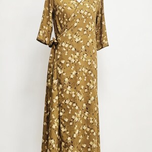 May include: A long, olive-green wrap dress with a floral pattern. The dress features a V-neck, three-quarter sleeves, and a tie closure at the waist. The fabric is covered in small, white and cream-colored flowers.
