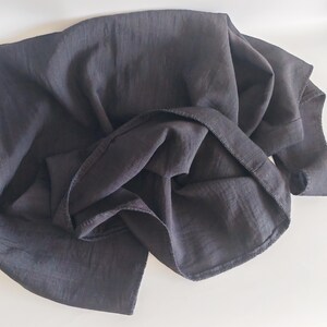 May include: A dark gray fabric, possibly linen or a similar material, is draped and folded, creating soft shadows and textures. The fabric's edges are visible, suggesting a garment or textile piece.