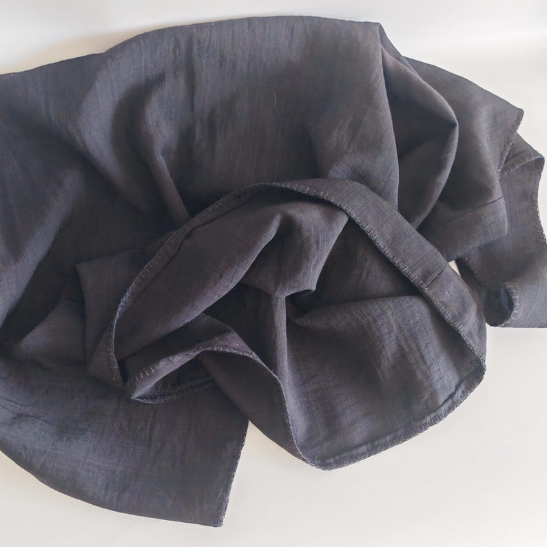 May include: A dark gray fabric, possibly linen or a similar material, is draped and folded, creating soft shadows and textures. The fabric's edges are visible, suggesting a garment or textile piece.