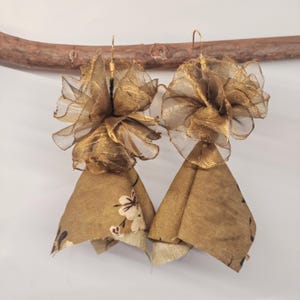 May include: A pair of handmade gold earrings. Each earring features a layered design with a sheer, ruffled top and a bell-shaped bottom. The bottom portion is a patterned fabric with white floral accents.