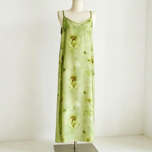 May include: A light green slip dress with a floral pattern. The dress has a V-neckline and spaghetti straps. The dress is displayed on a mannequin.