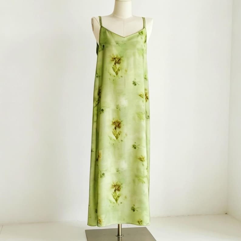 May include: A light green slip dress with a floral pattern. The dress has a V-neckline and spaghetti straps. The dress is displayed on a mannequin.