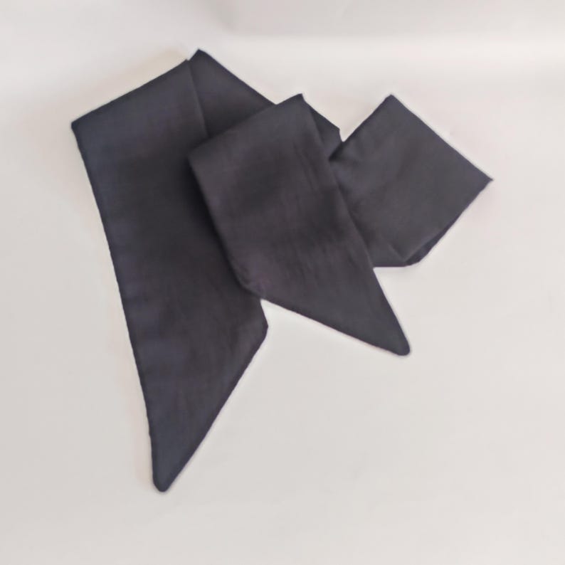 May include: A dark navy blue scarf, folded and arranged on a white surface. The scarf has a rectangular shape with pointed ends. The fabric appears to be soft and flowing, suggesting a lightweight material.