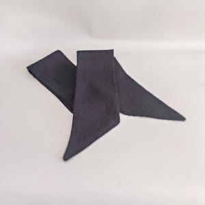 May include: A dark navy blue sash, likely made of fabric, is displayed against a white background. The sash is folded and has a triangular shape at the ends. The fabric appears to be smooth and opaque, with a slight sheen.