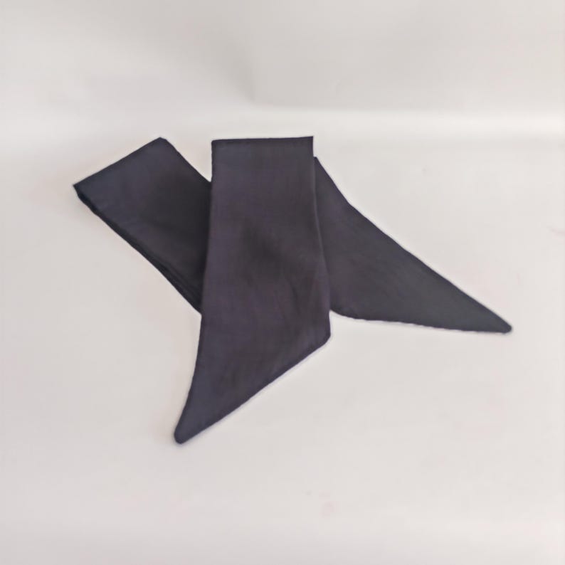 May include: A dark navy blue sash, likely made of fabric, is displayed against a white background. The sash is folded and has a triangular shape at the ends. The fabric appears to be smooth and opaque, with a slight sheen.