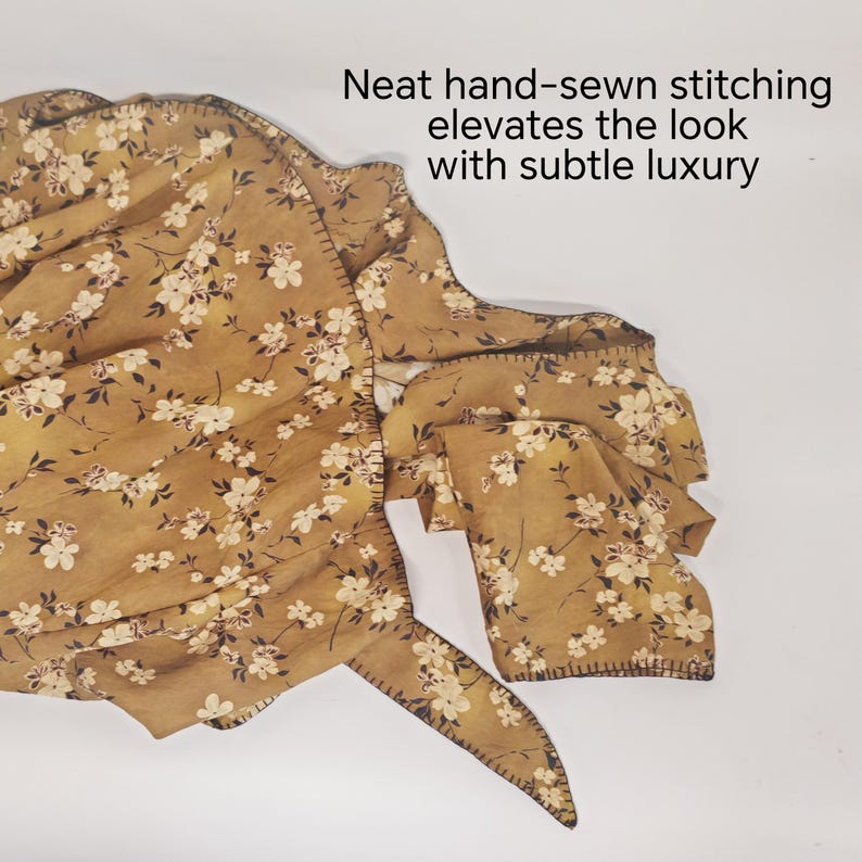 May include: Mustard-colored fabric with a floral pattern of white flowers and dark brown accents. The fabric has neat hand-sewn stitching around the edges. The text in the image reads: "Neat hand-sewn stitching elevates the look with subtle luxury."