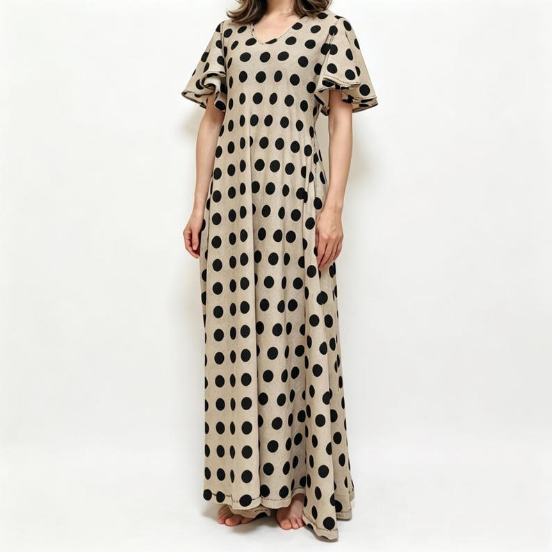 May include: A floor-length beige dress featuring a repeating pattern of large black polka dots, a V-neckline, and short, flared flutter sleeves. The garment has a loose, flowing silhouette that extends to the floor, covering the lower legs.