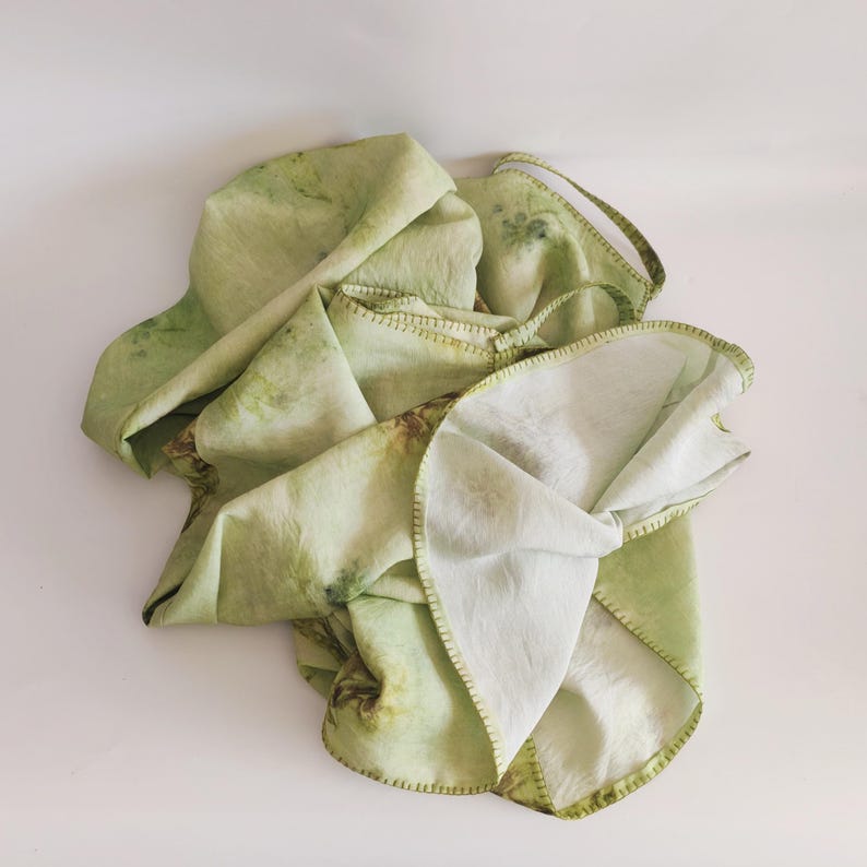 May include: A light green, botanical-print textile with a stitched border. The fabric has a layered appearance, with visible seams and a natural, organic aesthetic. The textile features a mix of light and dark green hues.
