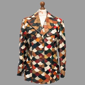 May include: A vintage jacket with a unique patchwork design. The jacket features a variety of colors, including brown, black, red, and white, arranged in a scale-like pattern. It has a collared neckline, button closure, and two front pockets. The jacket is displayed on a mannequin.