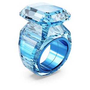 Puede incluir: Un gran anillo de piedra preciosa azul claro con una parte superior rectangular y un diseño facetado. El anillo tiene una banda azul y una apariencia cristalina clara, creando un efecto visual llamativo. El anillo está sobre un fondo blanco.