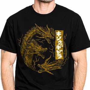 May include: Black t-shirt featuring a gold illustration of a three-headed dragon in a circular design. The shirt includes Japanese text in a vertical rectangle. The design is centered on the chest.