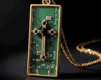 Op de afbeelding: Een goudkleurige hangerketting. De hanger heeft een rechthoekige gouden lijst met een groene printplaat. Een gouden kruis met zwarte accenten is gecentreerd op de plaat. De ketting heeft een fijne gouden ketting.
