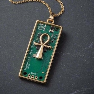 Könnte beinhalten: Goldfarbene Halskette mit Anhänger, der ein grünes Leiterplattendesign und ein goldenes Ankh-Symbol aufweist. Der rechteckige Anhänger trägt den Text "Raspberry Pi Pico © 2020" und "DEBUG". Die Kette ist ebenfalls goldfarben. Der Anhänger ist ca. 4 cm lang.
